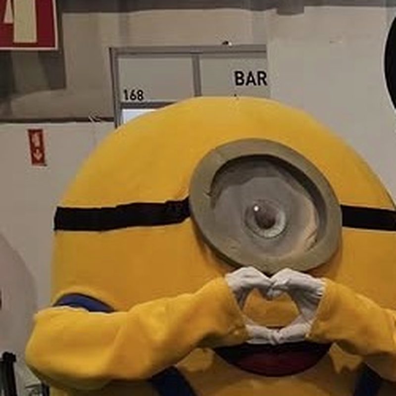 Mascote do Minion em fato a fazer um coração com as mãos